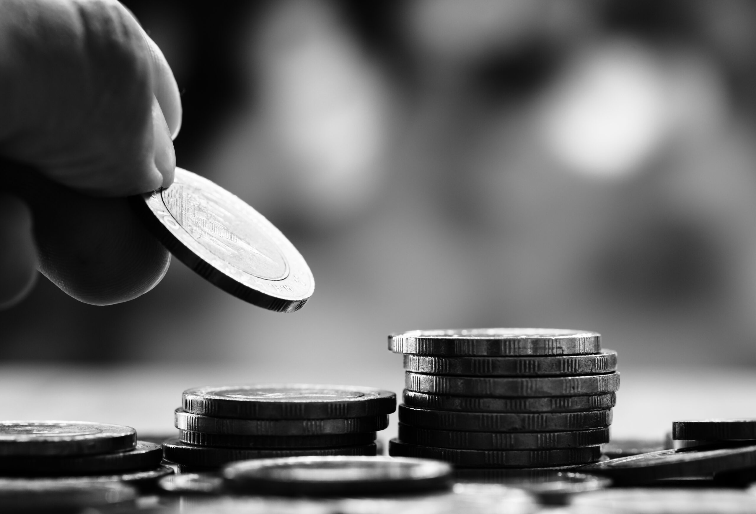 Multiple piles of coins, with a hand adding one more coin to the pile.